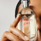 Hand holding a Tommy Hilfiger 'Tommy Girl' perfume bottle against a neutral background